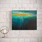 Abstract painting Beneath with blue and gold tones on a white brick wall