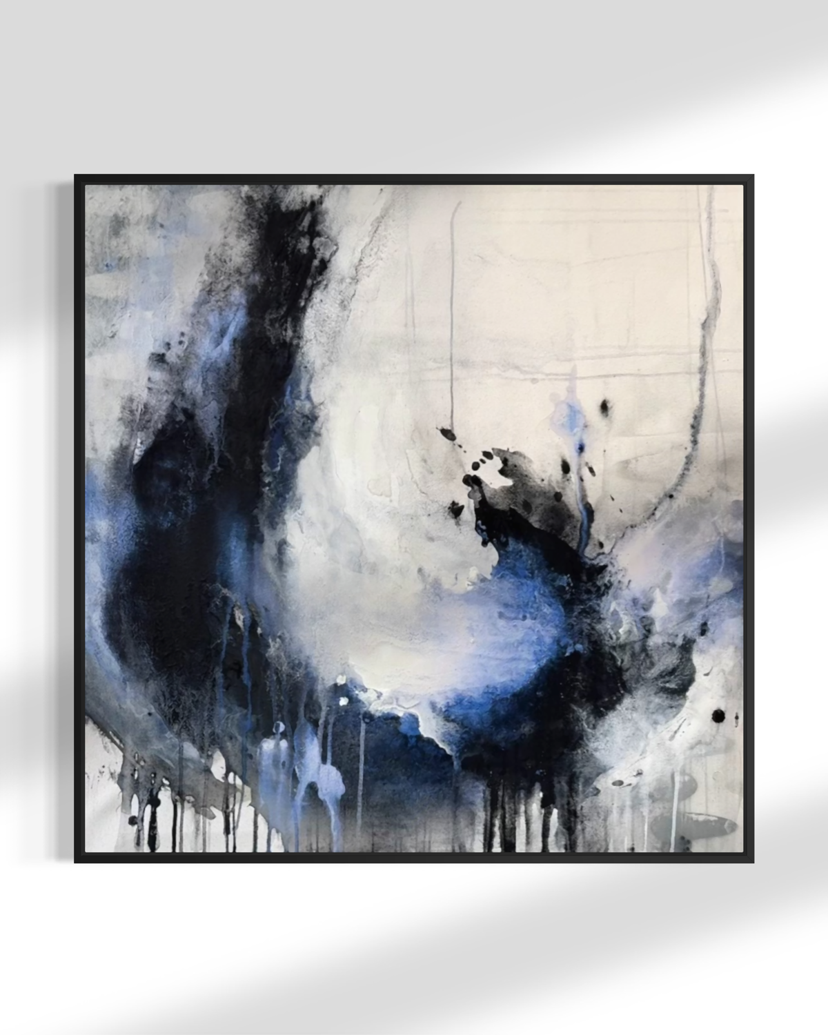 Abstract framed wall art featuring expressive black, white, and blue paint drips and splashes, displayed against a light gray wall. Charcoal and acrylic energy bloom by jen muse.