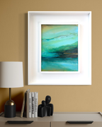 Framed abstract wall art hanging on a beige wall above a console table with a lamp, books, and small figurines. The artwork features layered teal, aqua, green, and dark blue brushstrokes inside a white frame by artist jen muse.