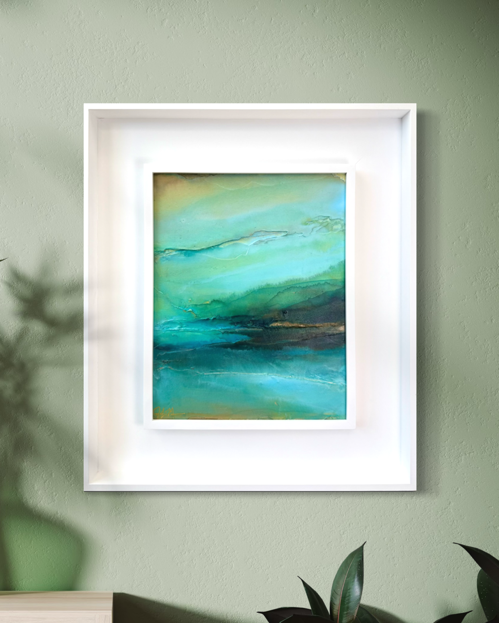 A framed, modern, abstract landscape painting with shades of teal, green, and blue, displayed in a white frame on a sage green wall by artist Jen Muse
